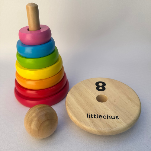 A wooden stacking ring toy set with colorful rings in pink, blue, green, yellow, orange, and red, a round wooden base printed with the number 8 and the name 'littlechus', and a small wooden ball on a light neutral background.